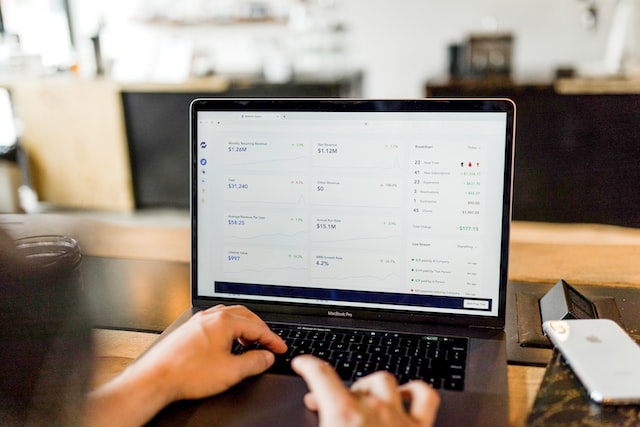 an over-shoulder shot of a person using a laptop, the screen shows a financial dashboard of revenue, recurring revenue, and so on