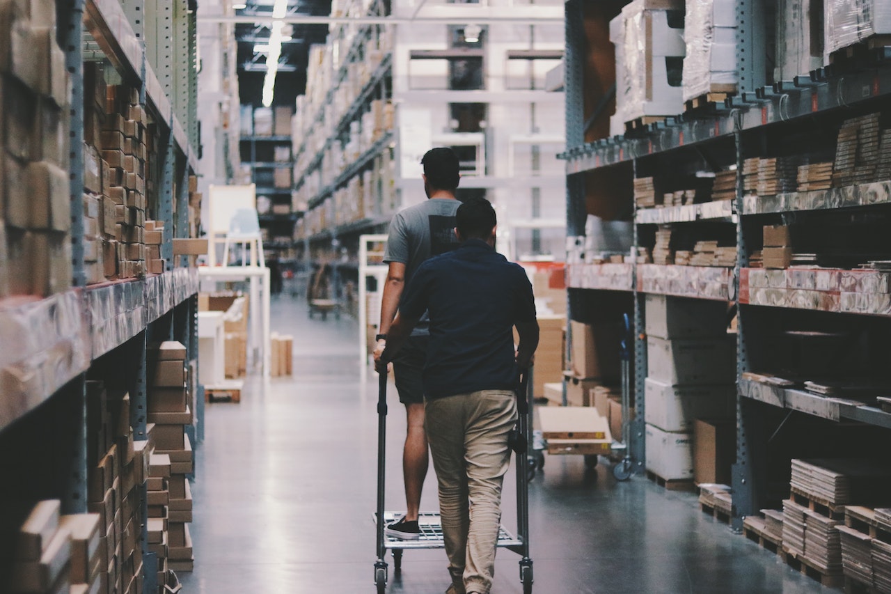 Two men in a warehouse with tall shelves walk away from camera