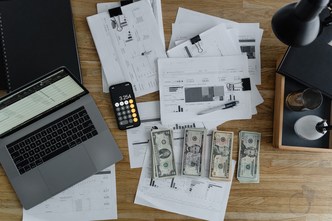payroll an overheard shot of an open laptop next to spreadsheet print outs and neat piles of cash