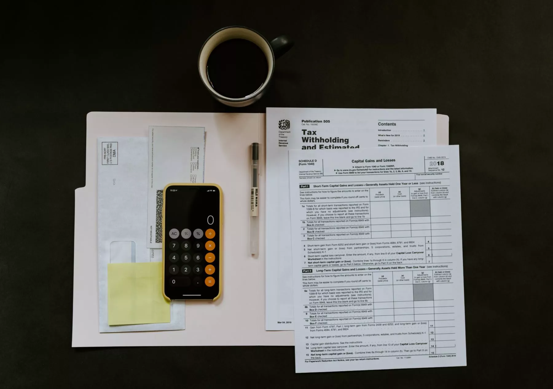 An open folder with several tax forms and a smartphone open to the calculator app