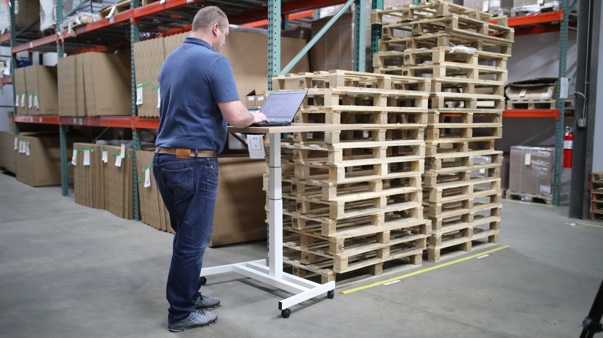 A man uses at a standing desk in the middle of a warehouse