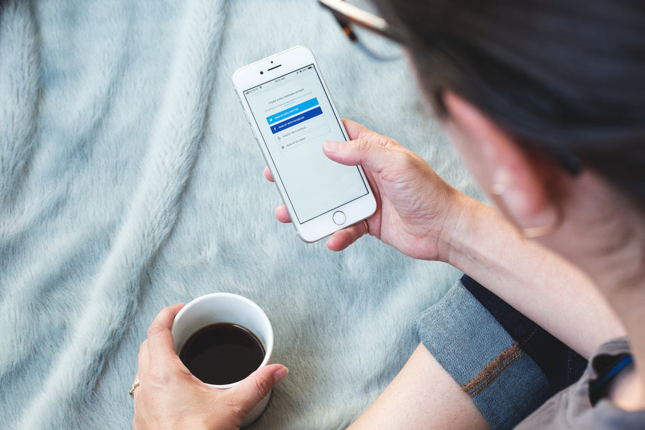 A woman holds a phone in one hand and a coffee in another, she is logging into Hootsuite