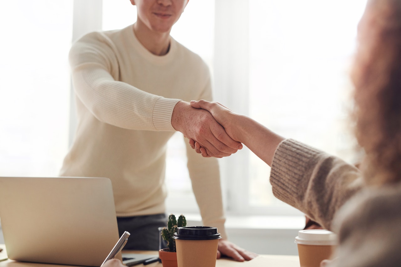 A man is standing behind a desk and reaching out to shake hands with a seated client